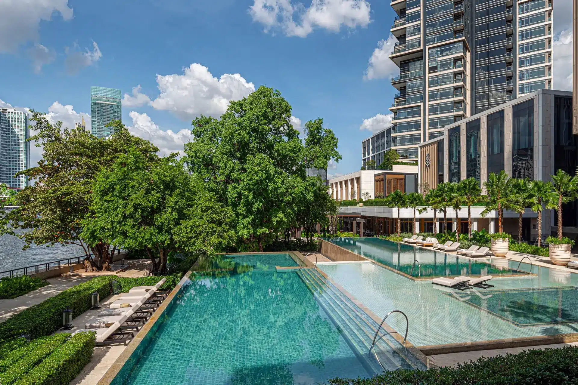 Outdoor pool and landscaped courtyards at Four Seasons Hotel Bangkok, with the riverfront hotel tower behind.