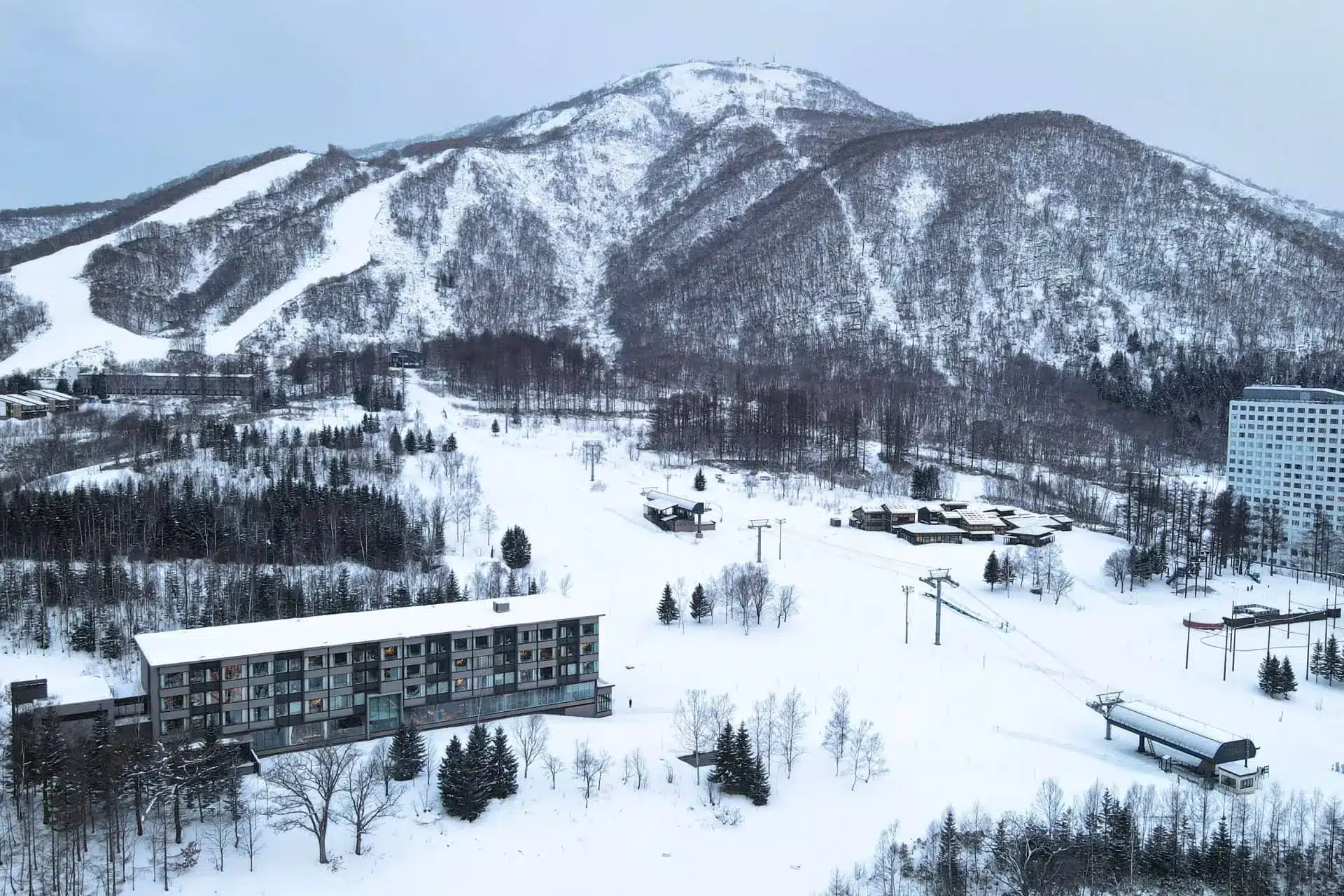 Snow-covered ski resort beneath a wooded mountain with hotels and chairlifts