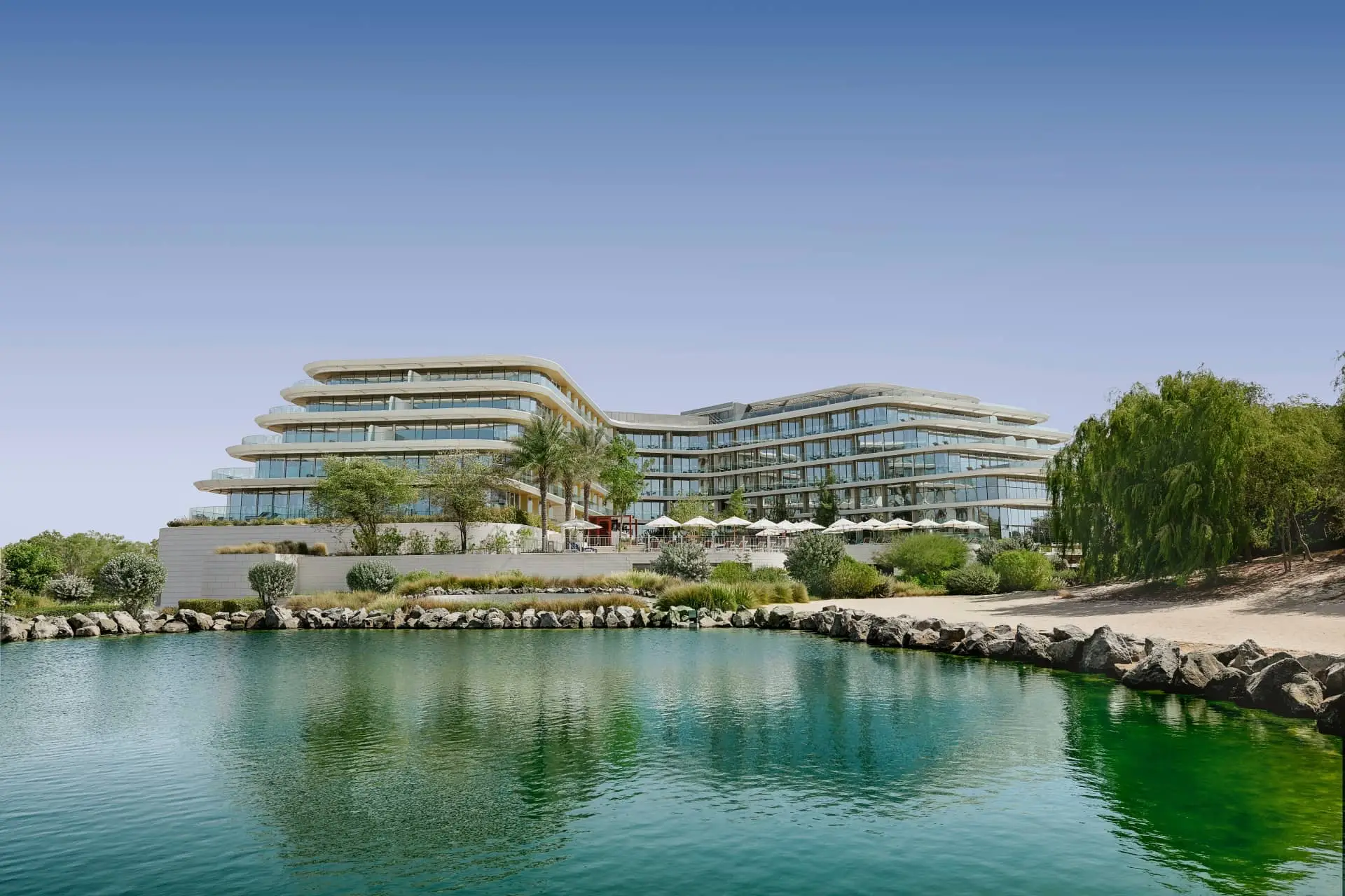 JA Lake View Hotel beside the marina, with landscaped grounds and palm trees reflected in the water.