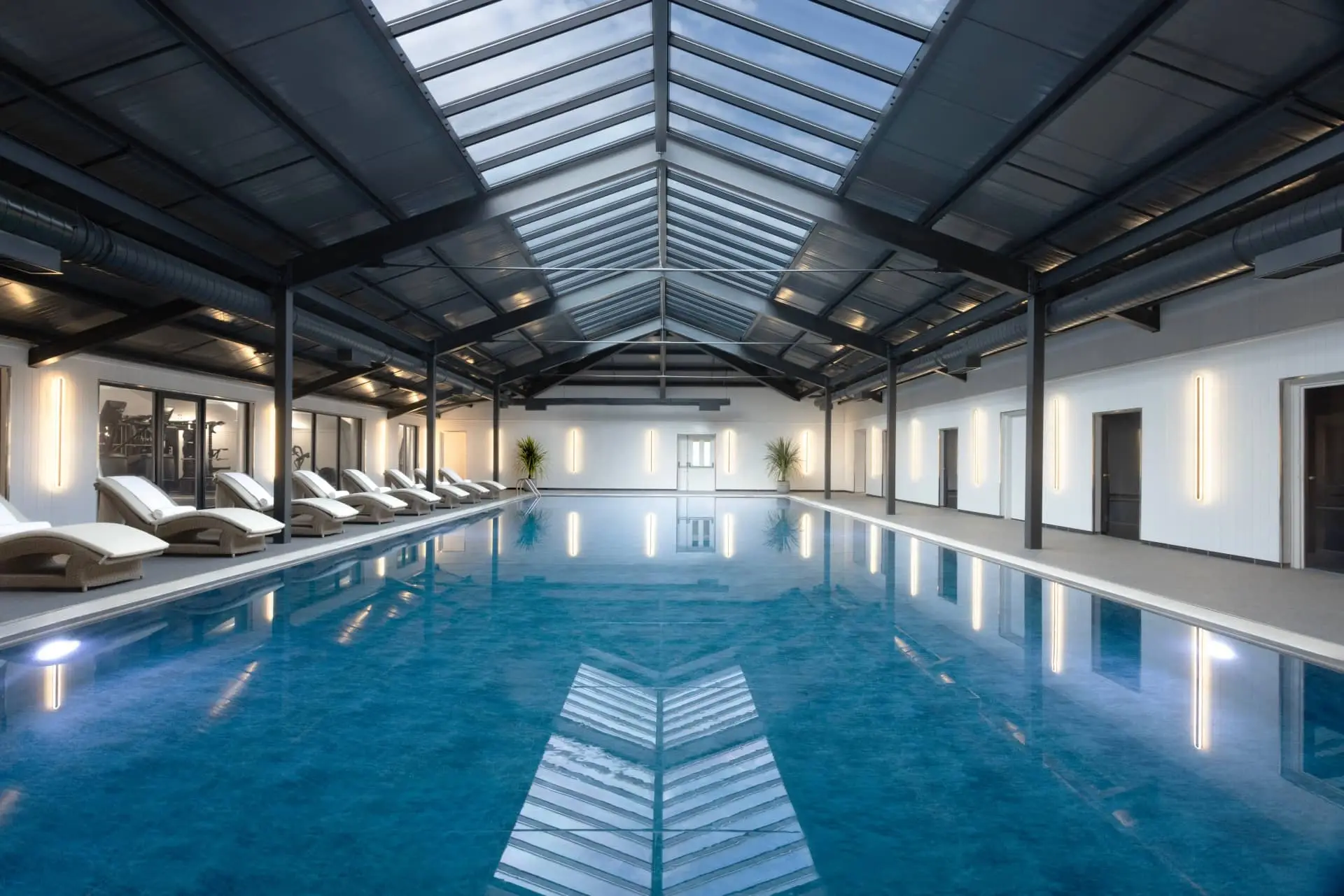 Luxury indoor swimming pool beneath a glass roof with loungers and spa-style interiors