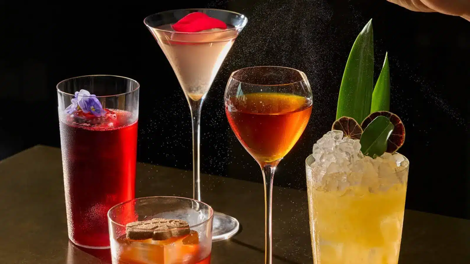 A selection of colorful cocktails with fruit garnishes arranged on a dark bar