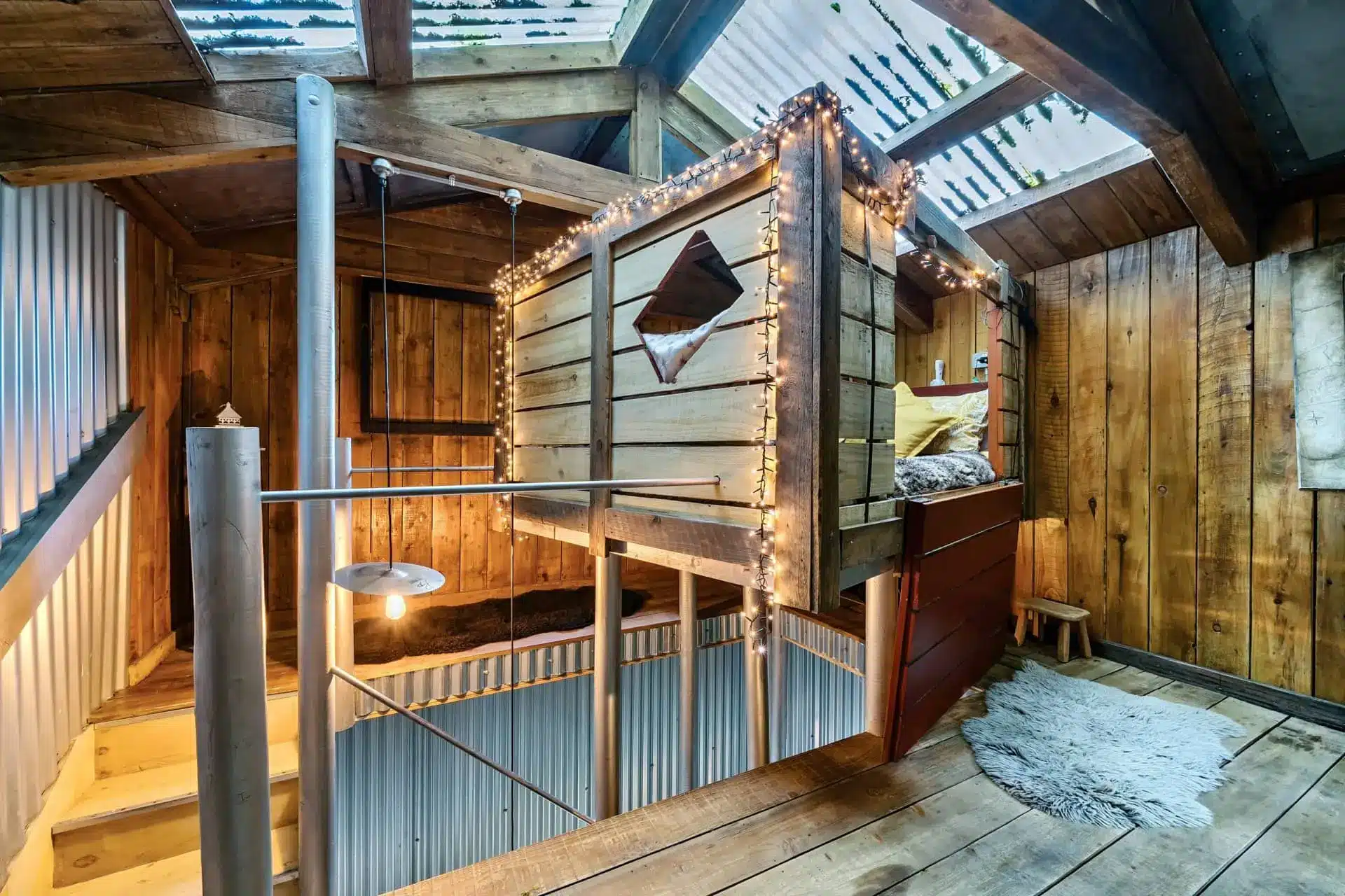 Multi-level interior of Humble Bee with a winding staircase, timber walls, string lights and a bed in a loft