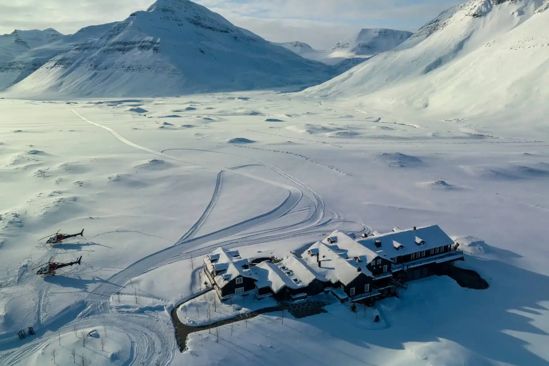 Deplar Farm, a turf-roofed lodge on Iceland’s Troll Peninsula, sits beside a snowy fjord beneath mountains.
