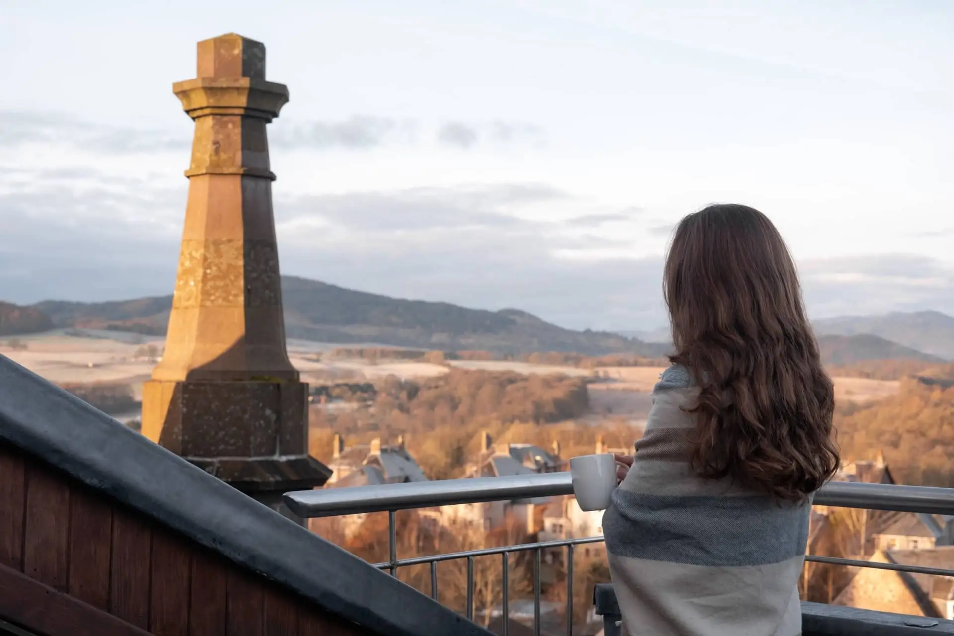 A woman looks out from the balcony of the Church Tower over autumn trees and hills.