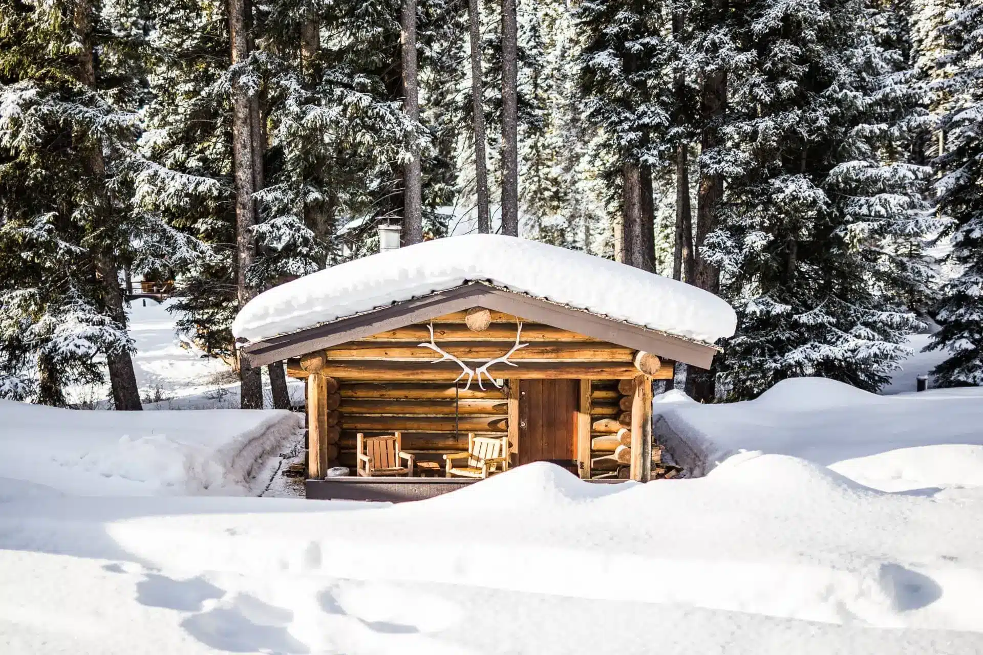 Snow-covered log cabin at Lone Mountain Ranch, with a timber porch and evergreen forest behind it.