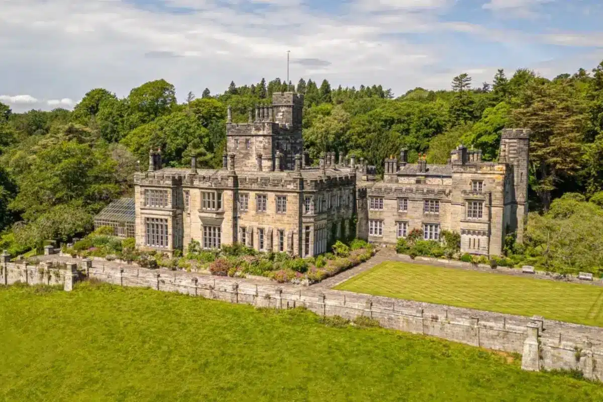 Grand stone castle surrounded by green lawns, trees, and a low garden wall