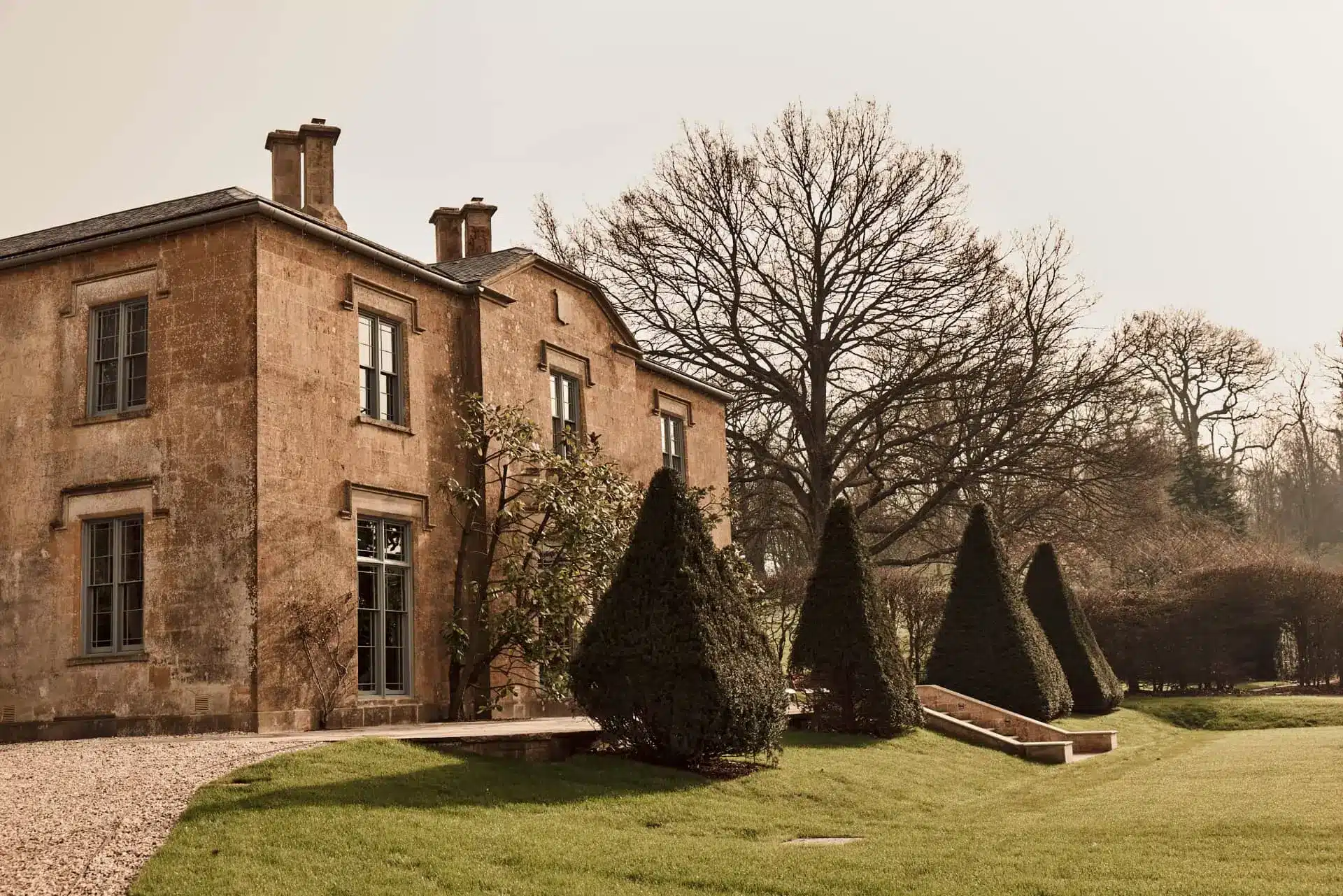 Yarlington Lodge’s brick main house, with a clipped hedge and bare trees in the lawn.