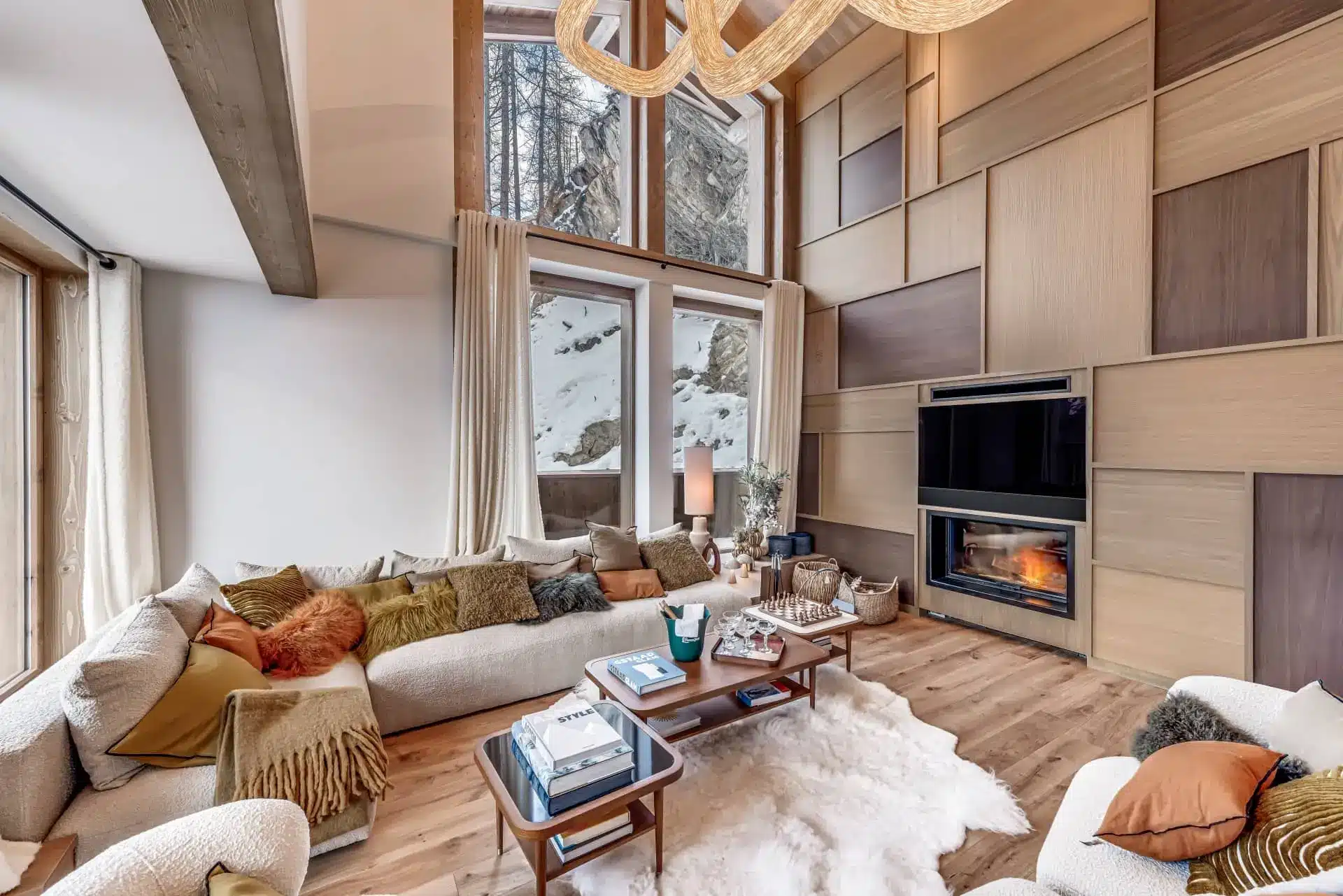 Chalet des Légendes’ bright living room, with a fireplace, sofas, coffee table and tall windows.