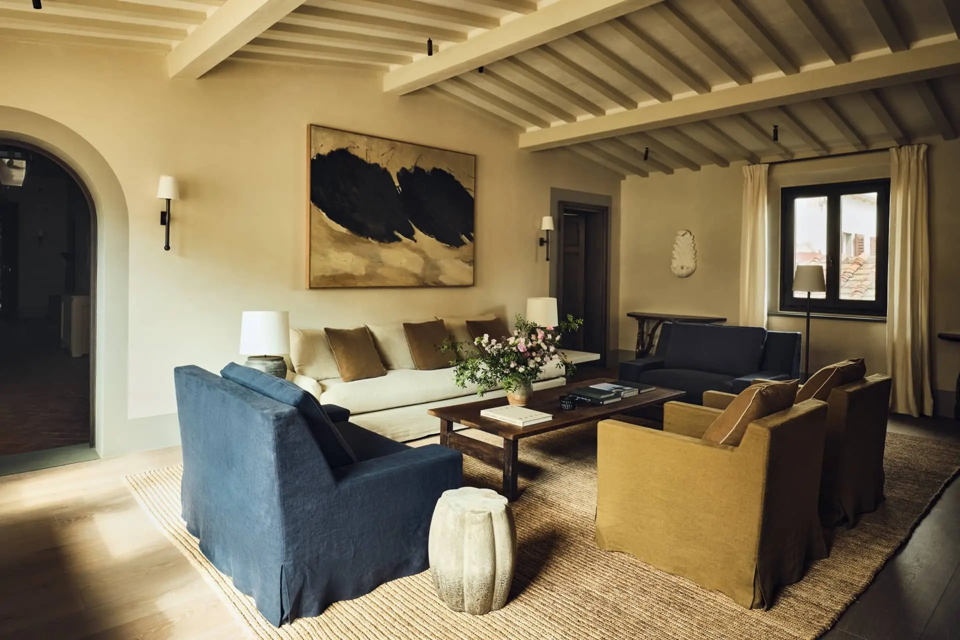 Living room at La Réserve Firenze, with blue armchairs, a cream sofa and exposed ceiling beams.