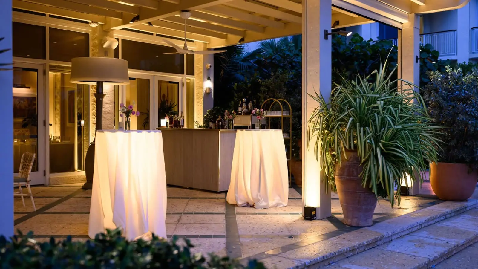 Florie’s ocean-view terrace set with a dining table and chairs, potted plants and warm lighting.
