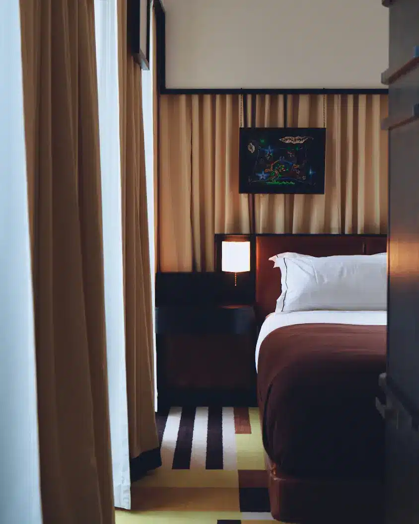 Guestroom at The Warbler Hotel with a king bed, striped wall, bedside table and dark wood furnishings.