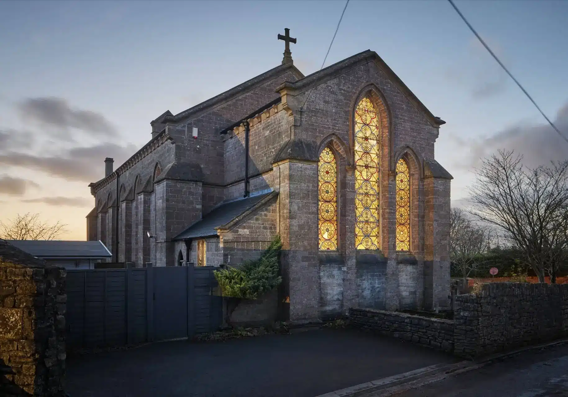 Exterior of the Gothic Church, a stone church with tall glowing stained-glass windows and a cross on its roof.