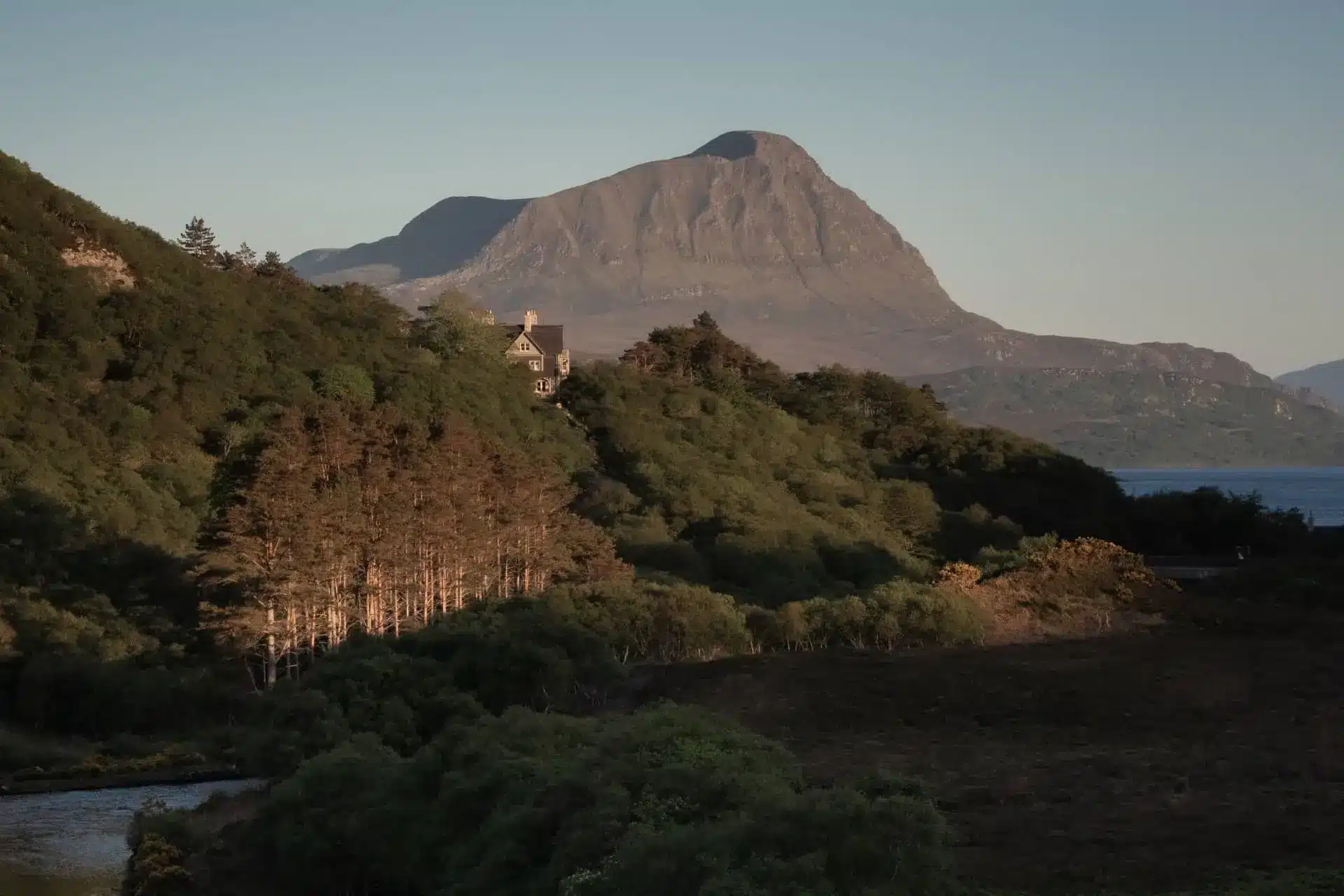 Hope Lodge sits among wooded hills above a loch, with a distant mountain rising behind it.