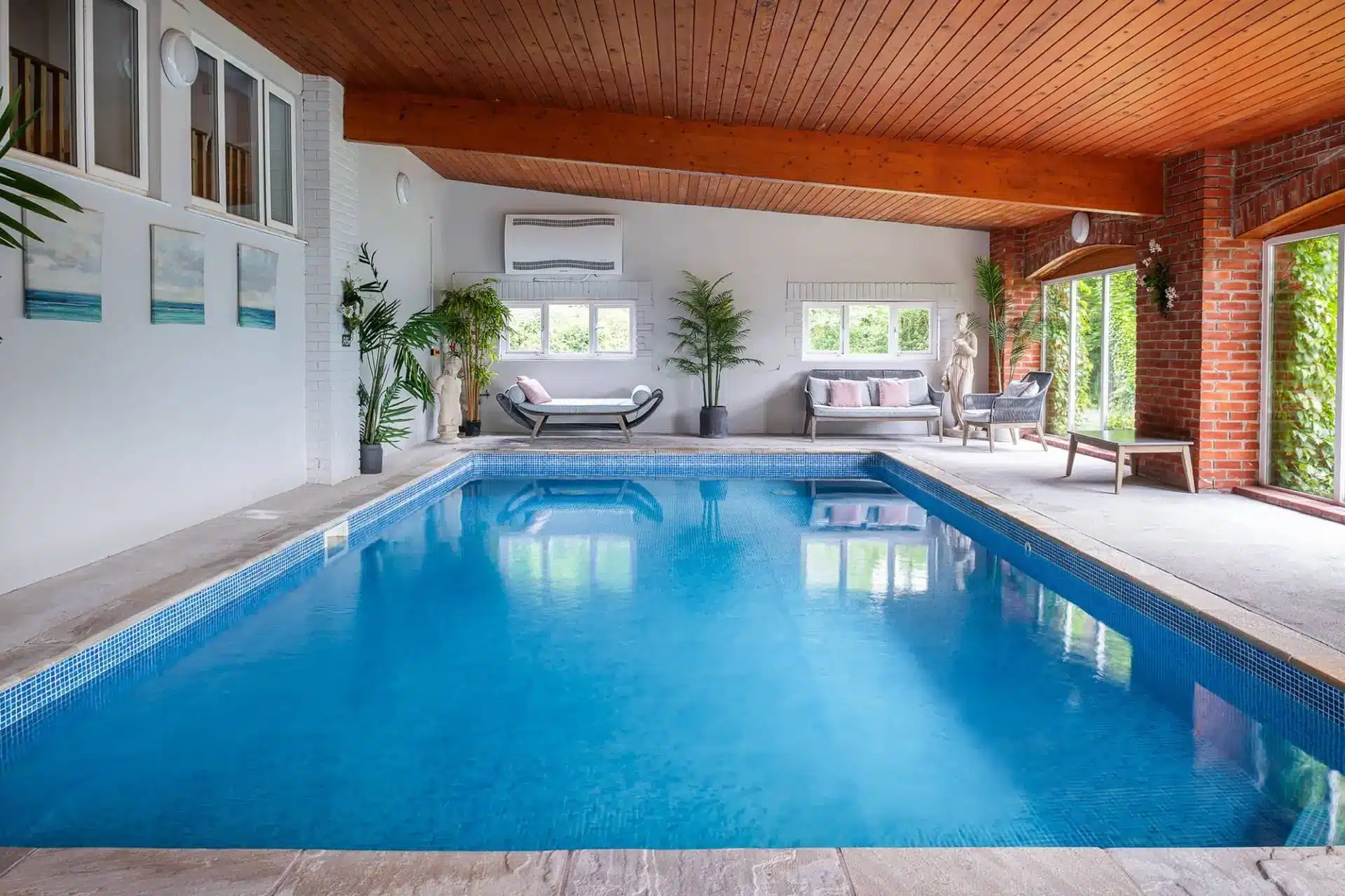 Indoor swimming pool at Aylesbury Cottage, with blue water, lounge seating and large windows.