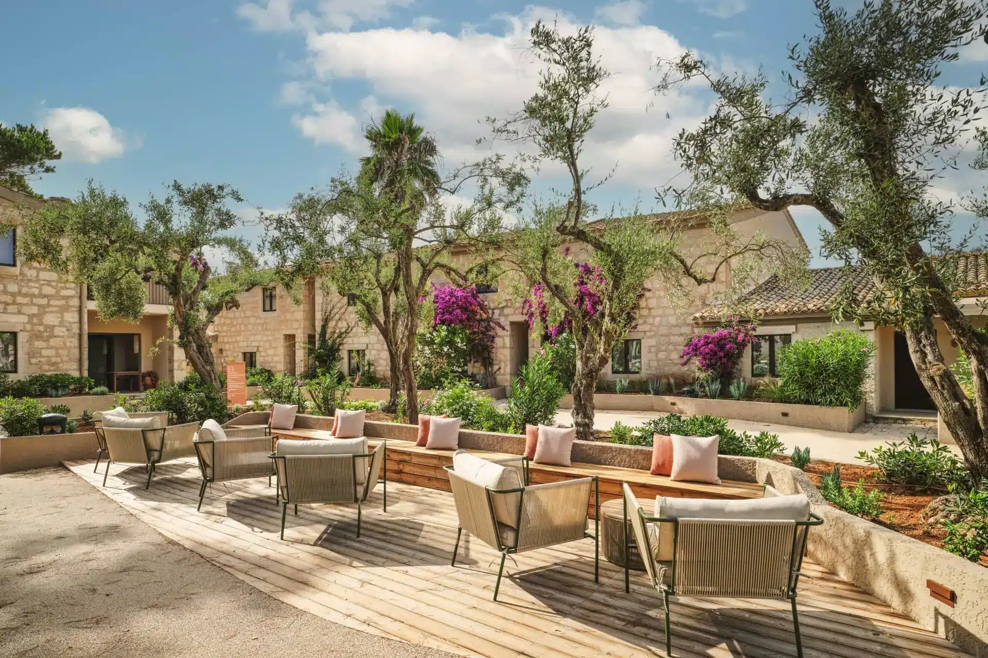 Outdoor lounge with low sofas and chairs on a timber deck beside landscaped resort buildings