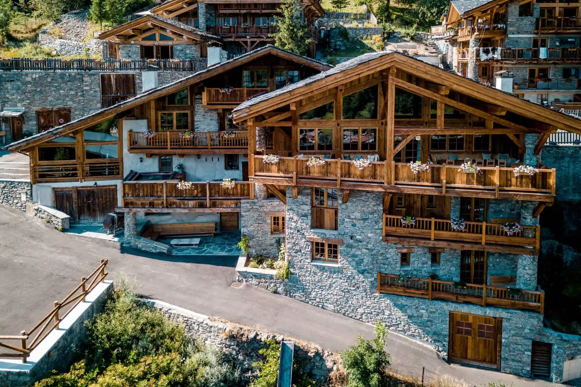 Snow-covered Alpine chalets with steep roofs and wooden balconies sit above a winding mountain road.
