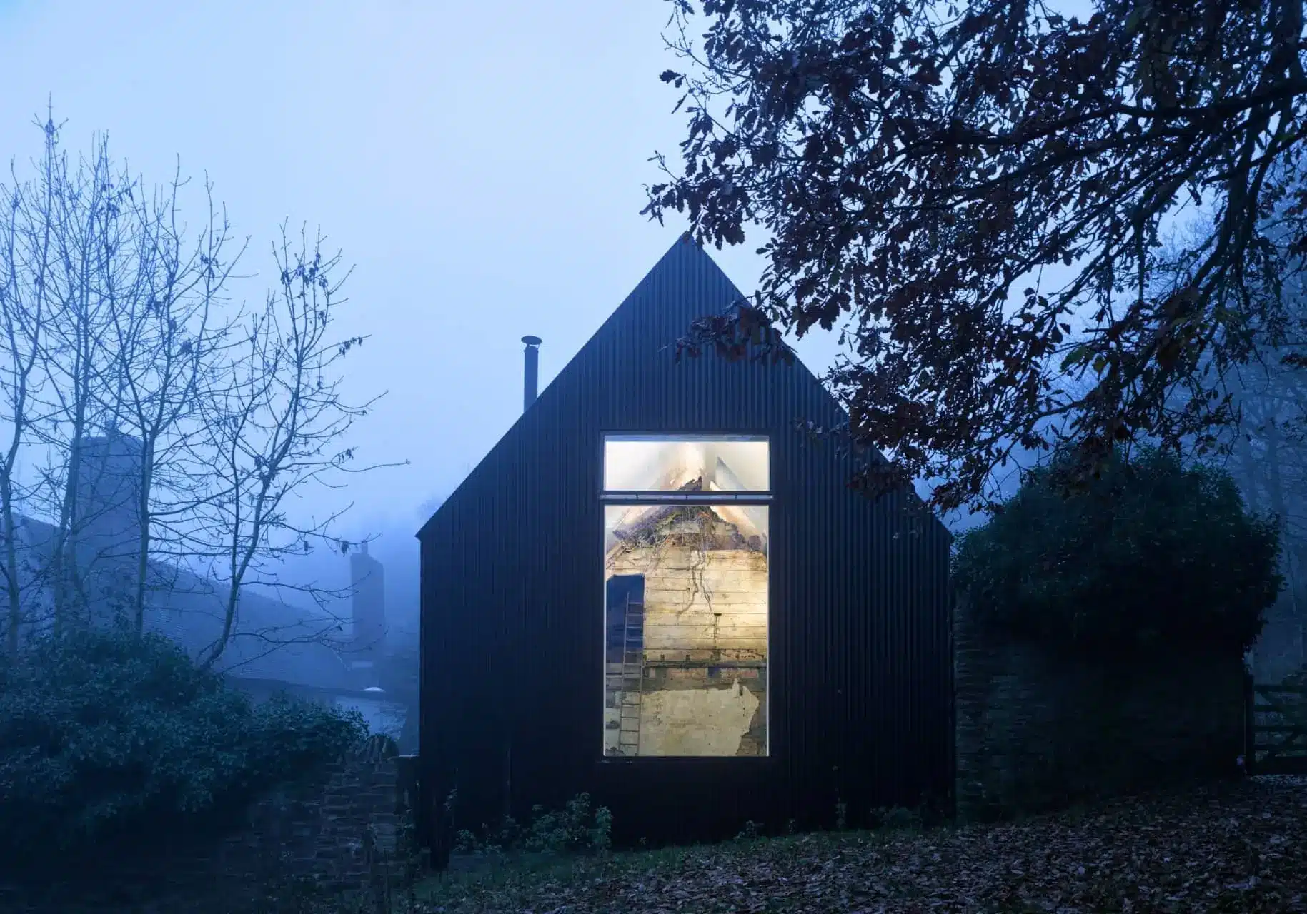 Croft Lodge Studio at dusk, its old cottage enclosed by a dark corrugated-metal shell with a warmly lit window.